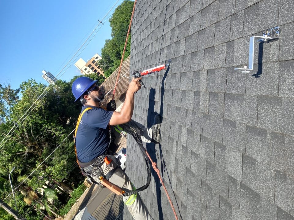 Instalador da Perfect preso por corda, fixando o suporte das placas em telhado de shingle